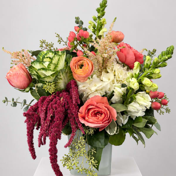 Mixed bouquet with coral roses, white blooms, and green snapdragons in a glass vase