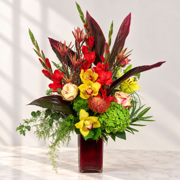 Bright tropical bouquet in a red glass vase with yellow orchids and red blooms