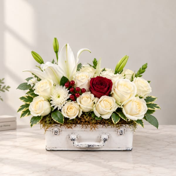 White lilies and roses arranged in a white suitcase-style container