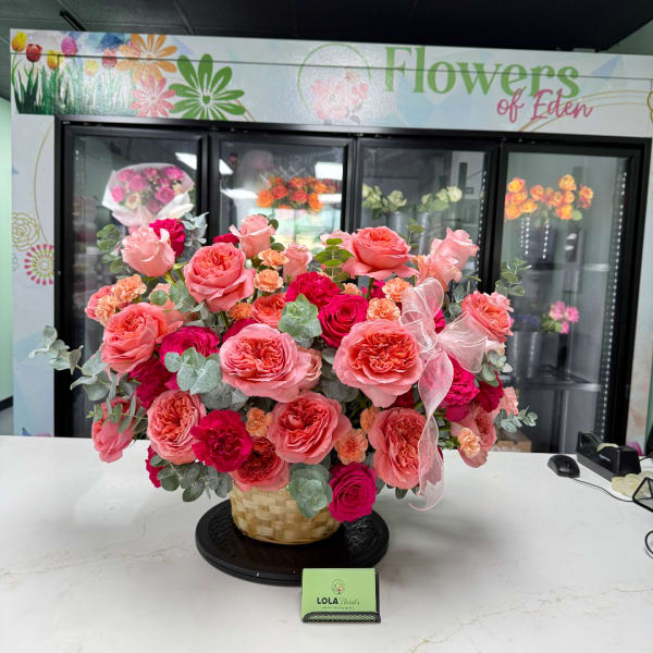 Pink and coral rose arrangement in a woven basket with a ribbon bow.