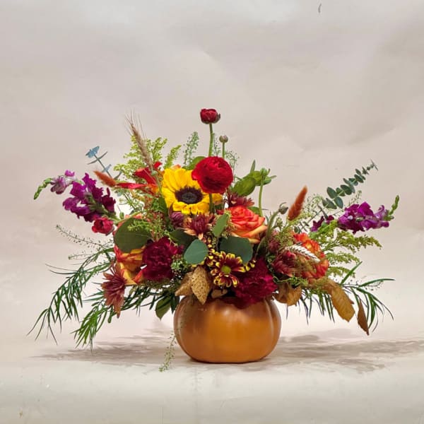 Mixed autumn bouquet in a pumpkin-shaped vase with sunflowers, roses, and purple blooms