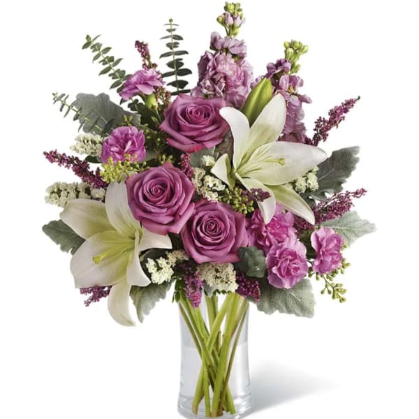 Purple roses and white lilies in a clear glass vase