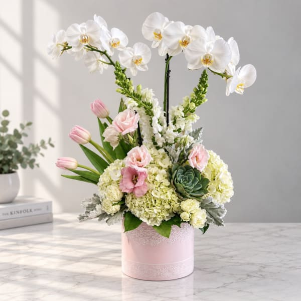 Pink and white floral arrangement in a pink box with orchids and tulips