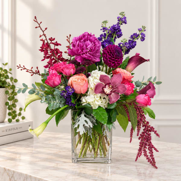Mixed bouquet of pink, purple, and white flowers in a clear glass vase