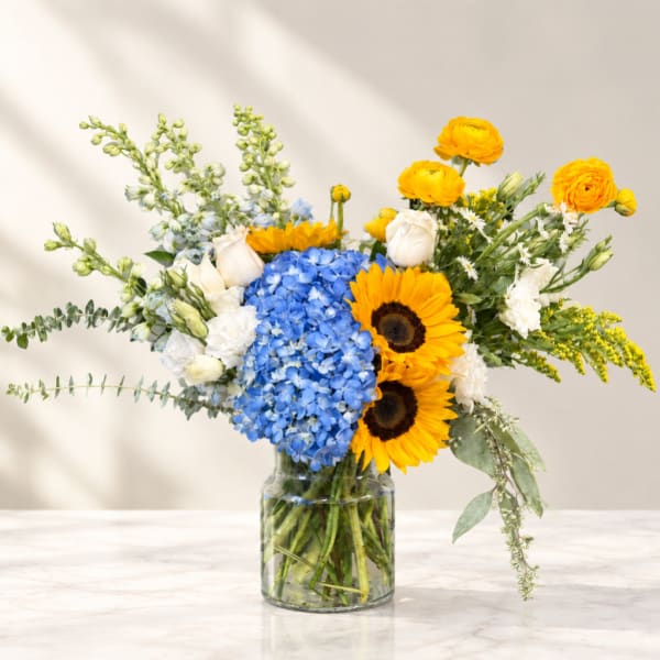 Bouquet of blue hydrangea, sunflowers, and white roses in a glass vase
