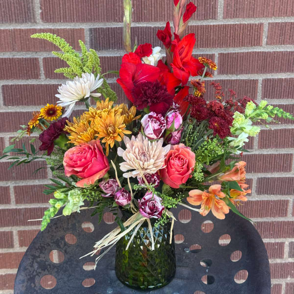 Mixed bouquet in a green glass vase with red, pink, white, and orange flowers.