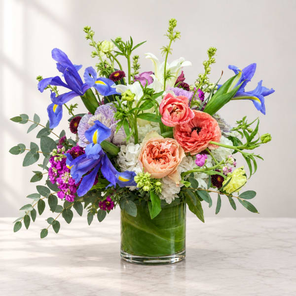 Colorful bouquet of irises, roses, and lilies in a clear glass vase