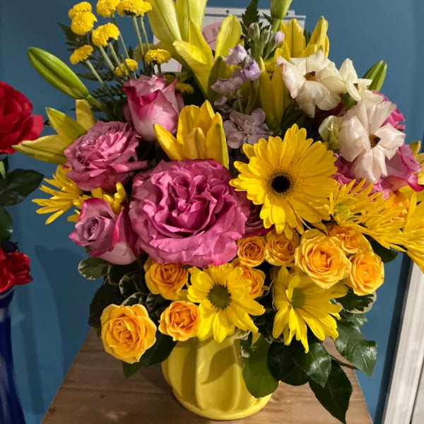 Mixed bouquet of pink, yellow, and white flowers in a yellow vase