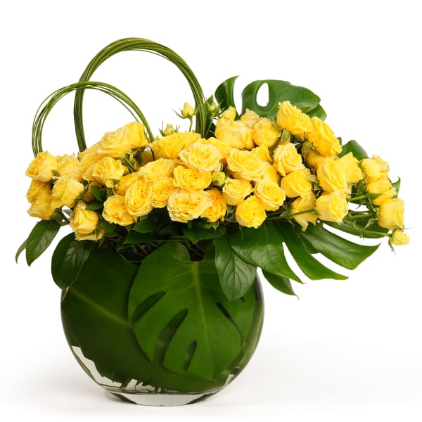 Yellow roses in a green glass vase with large tropical leaves