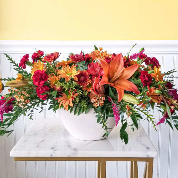 Long floral arrangement in a white bowl with orange lilies and red-orange blooms