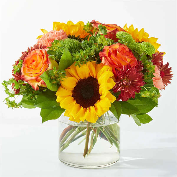 Bouquet of sunflowers, roses, and chrysanthemums in a clear glass vase