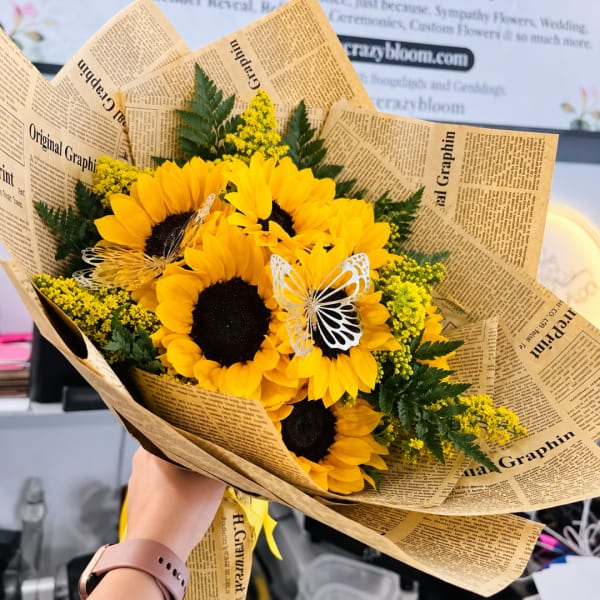 Bouquet of sunflowers wrapped in newspaper-style paper with butterfly accents.