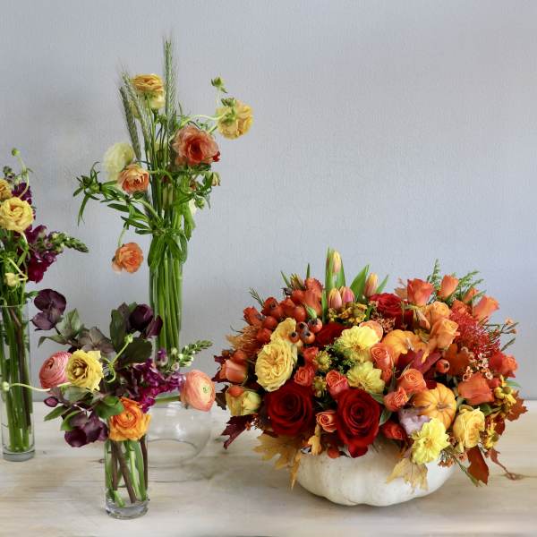 Autumn centerpiece of orange and yellow flowers in a white pumpkin with three smaller mixed bud vases.