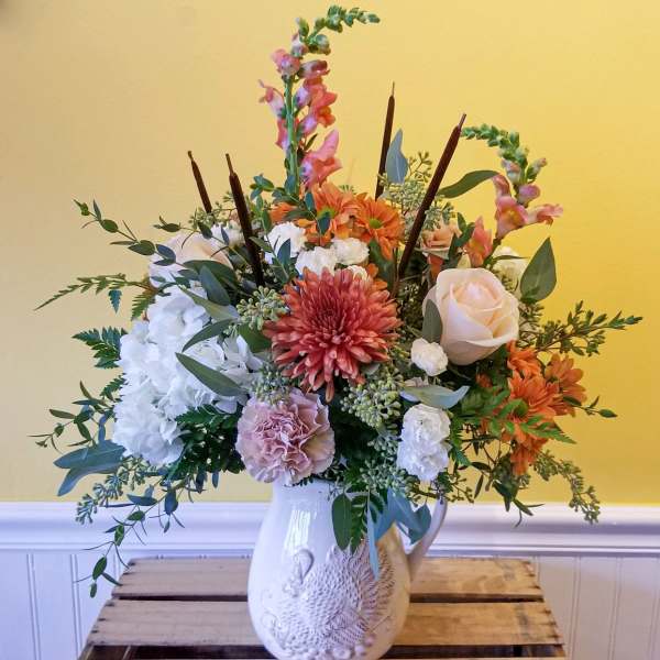 Mixed floral arrangement in a white ceramic pitcher vase