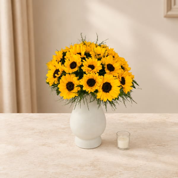 Yellow sunflowers arranged in a white vase with a small candle beside it