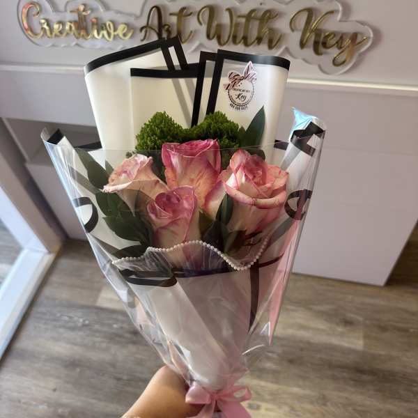 Handheld bouquet of pink roses wrapped in clear plastic with a pink ribbon