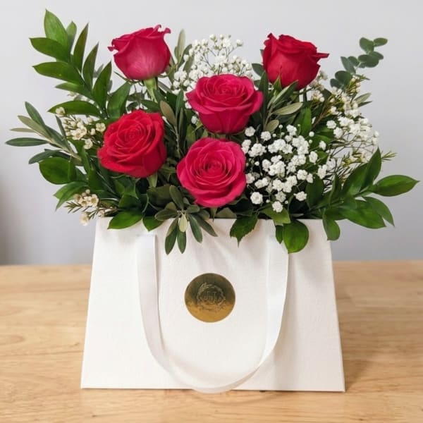 Pink and red roses with baby's breath in a white gift bag