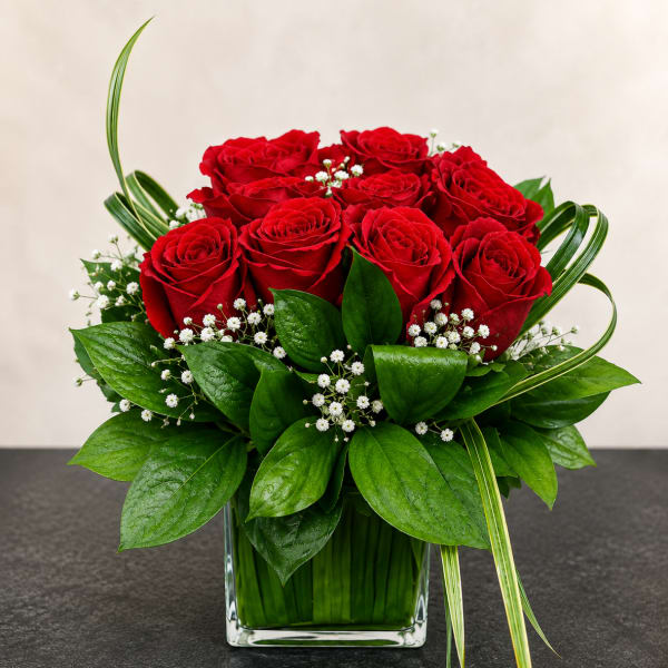 Red roses arranged in a clear square vase with white filler flowers