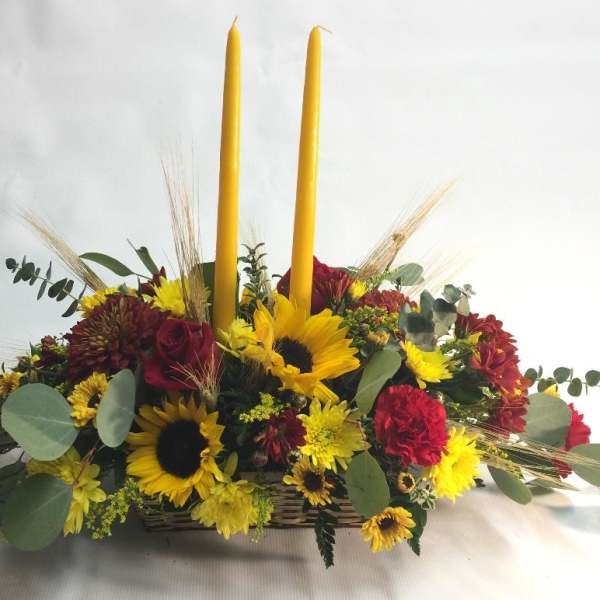 Sunflower and red flower arrangement with two tall yellow candles in a basket