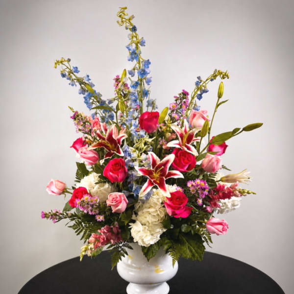 Tall mixed bouquet in a white vase with roses, lilies, and blue delphinium