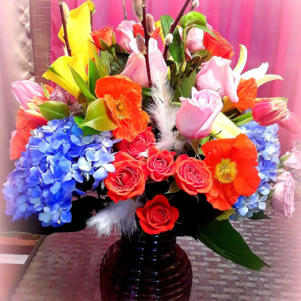 Colorful bouquet of roses, tulips, calla lilies, and hydrangeas in a dark vase