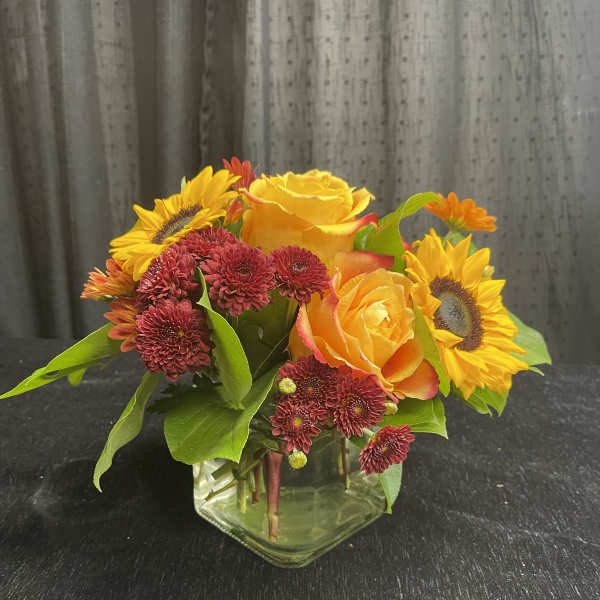Sunflowers, yellow roses, and burgundy mums in a clear glass vase