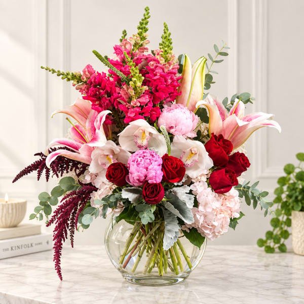 Mixed bouquet of pink, red, and white flowers in a clear glass vase