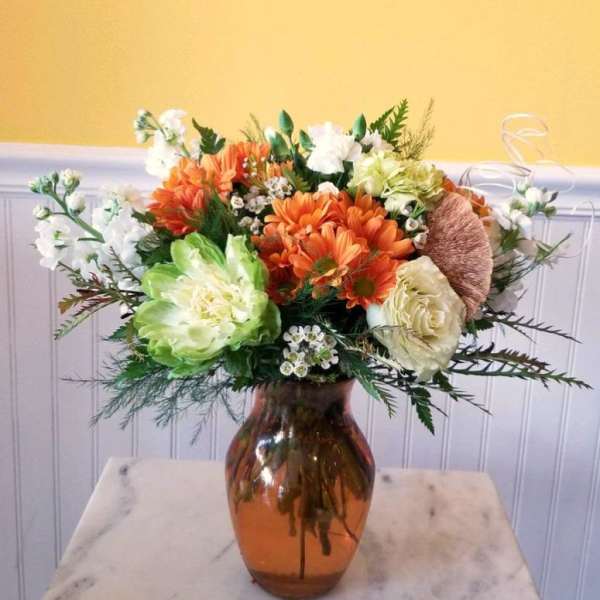 Orange and white flower arrangement in an amber glass vase