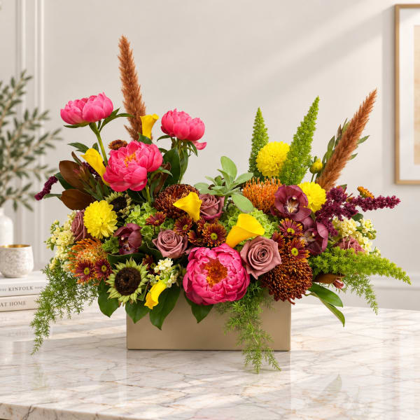 Colorful floral arrangement in a rectangular beige vase with pink, yellow, and burgundy blooms
