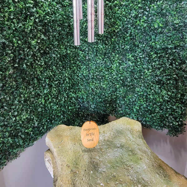 Wind chime hanging before a green foliage wall above a stone memorial marker