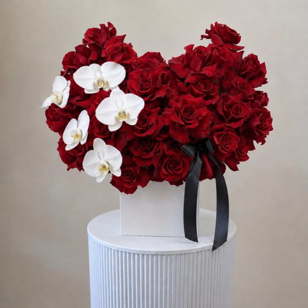 Red rose arrangement with white orchids in a white box and black ribbon