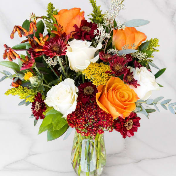 Bouquet of orange and white roses with burgundy daisies in a glass vase