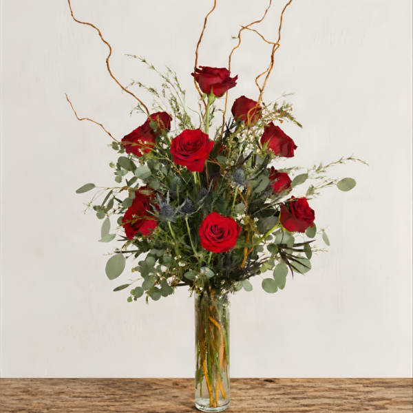 Red roses arranged in a tall glass vase with airy greenery