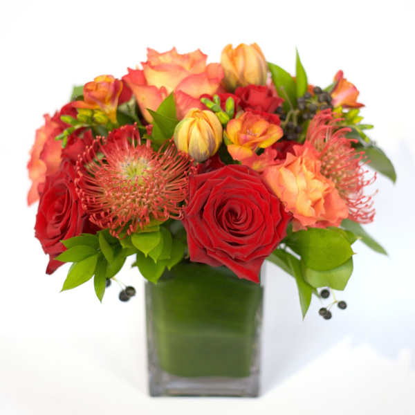 Red and orange floral arrangement in a square glass vase