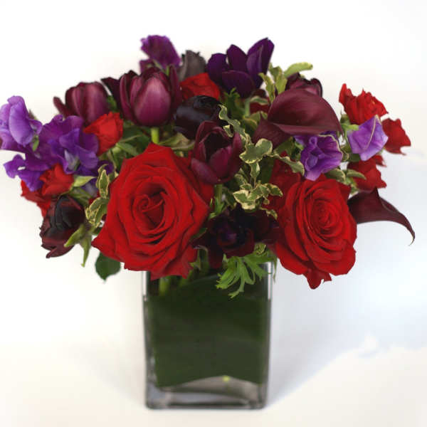 Red roses and purple flowers in a square glass vase