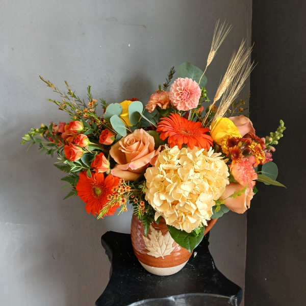 Mixed bouquet of orange, peach, yellow, and pink flowers in a ceramic vase