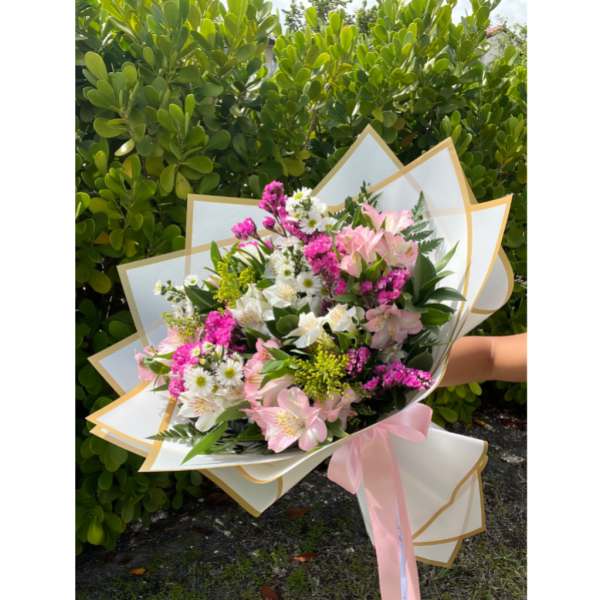 Handheld bouquet of pink and white flowers wrapped in white paper with a pink ribbon