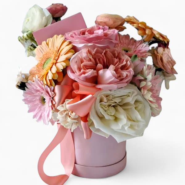 Pink and white mixed flowers arranged in a pink hatbox with a satin ribbon and card