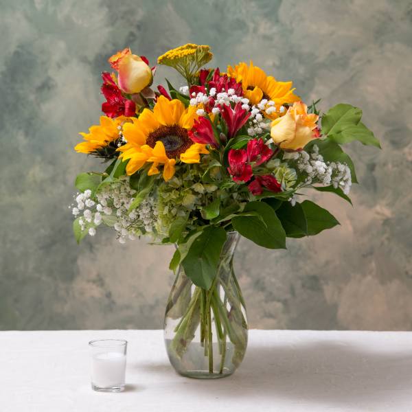 Mixed bouquet of sunflowers, roses, and red alstroemeria in a glass vase