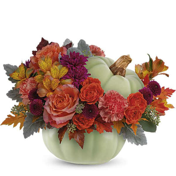 Low autumn bouquet of orange and burgundy flowers in a light green ceramic pumpkin container