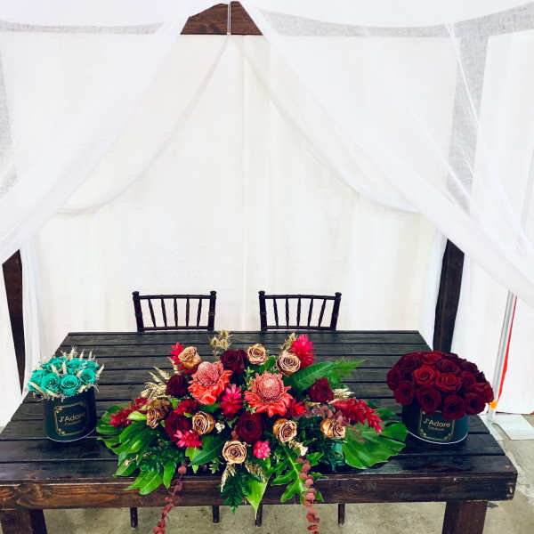 Three floral arrangements on a table, including red roses and turquoise roses in black containers