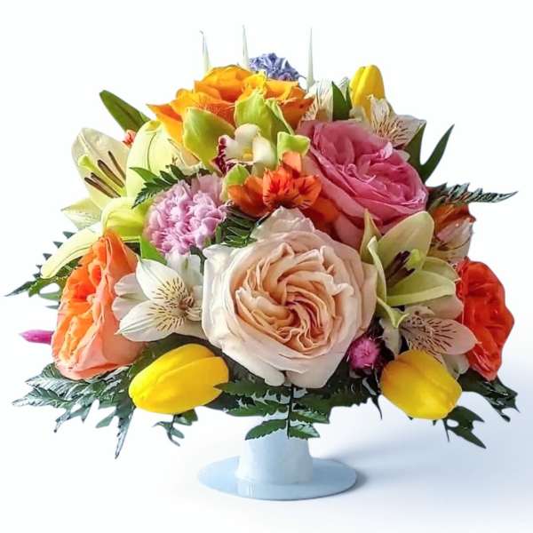 Mixed bouquet of roses, tulips, and lilies in a white pedestal vase
