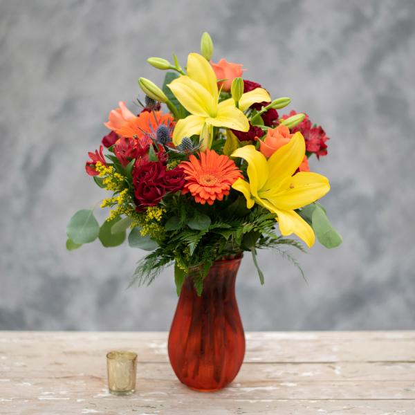 Mixed bouquet with yellow lilies, orange gerbera daisies, and red roses in a red vase