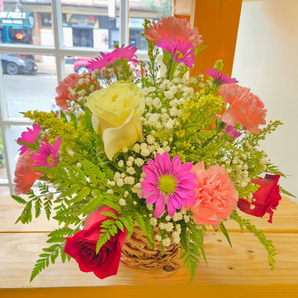 Mixed bouquet in a woven basket with roses, carnations, and daisies