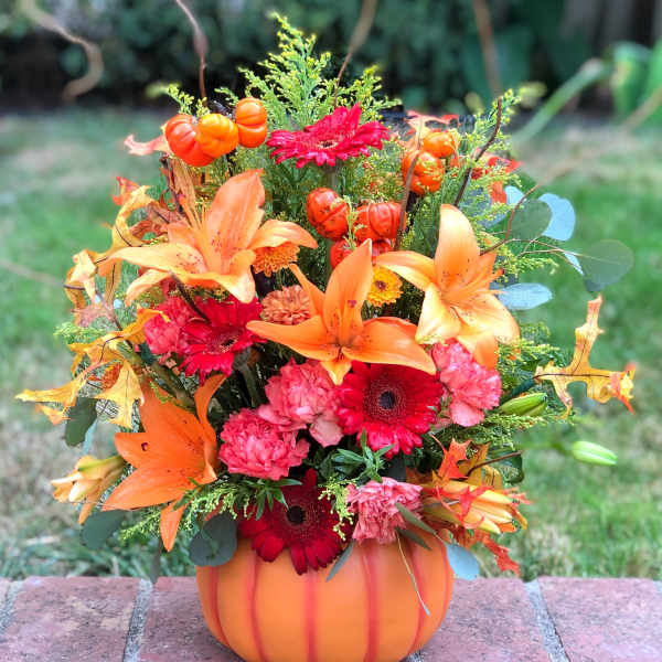 Autumn floral arrangement in a pumpkin-shaped container with orange lilies and red daisies