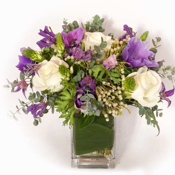 Purple and white flower bouquet in a clear square vase