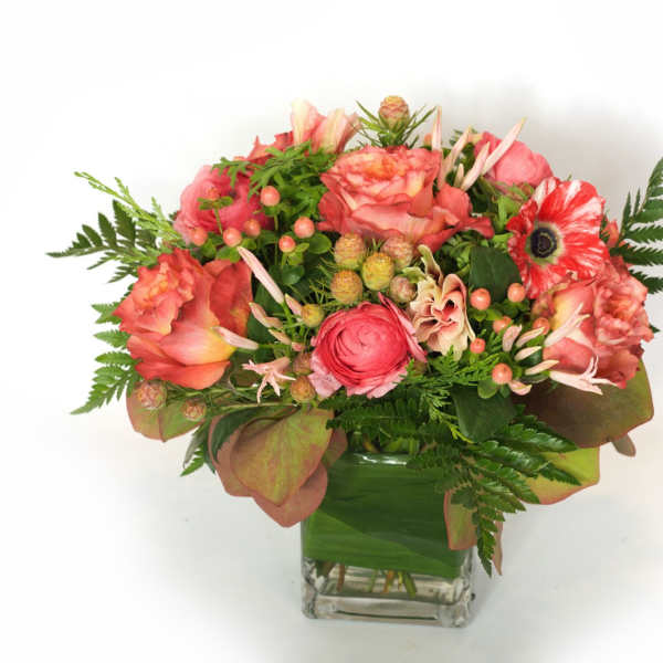 Pink and coral flower arrangement in a clear square vase