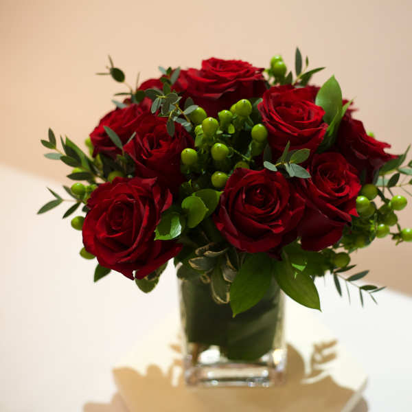 Red roses arranged in a clear glass vase with green berries
