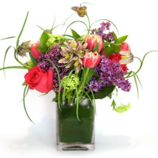 Mixed bouquet of red roses and purple flowers in a square glass vase