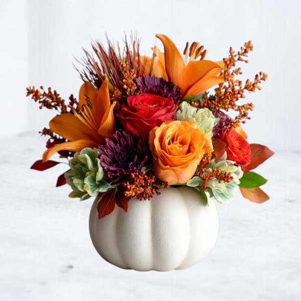 Orange and red floral arrangement in a white pumpkin vase